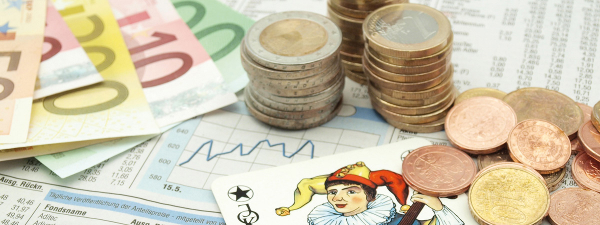 Ausschnitt mit Euromünzen und Scheinen sowie eines Aktien-Charts und einer Jokerkarte